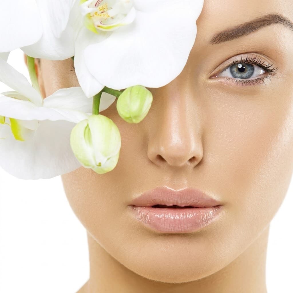 A woman with luminous skin beside white orchid blooms.